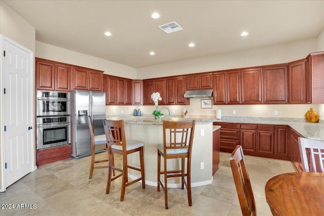 kitchen with light stone counters, a kitchen breakfast bar, a center island with sink, stainless steel appliances, and light tile flooring