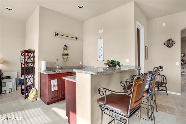 kitchen featuring kitchen peninsula, light tile flooring, a breakfast bar, sink, and light stone counters