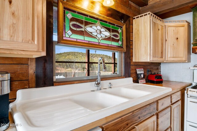 kitchen with light brown cabinetry, backsplash, white range oven, and sink