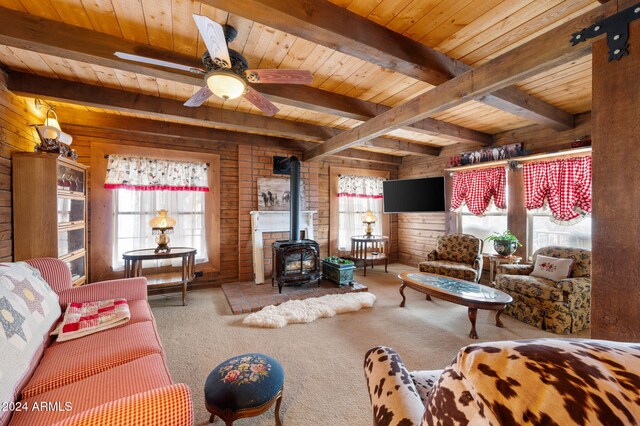 carpeted living room with a wood stove, ceiling fan, beamed ceiling, wooden walls, and wood ceiling