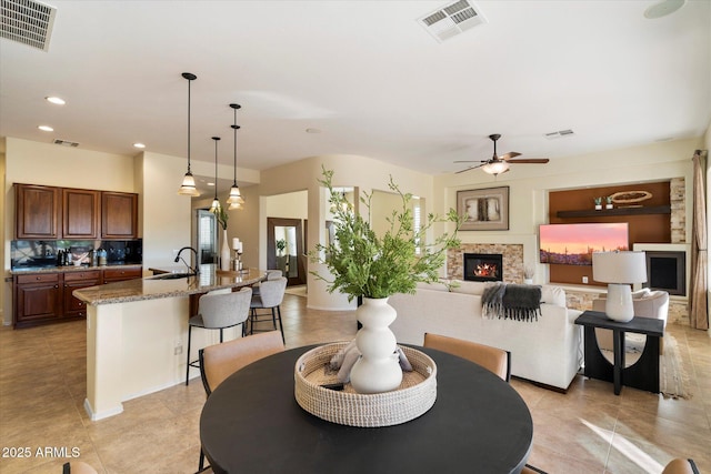 tiled dining room featuring ceiling fan, a stone fireplace, and sink