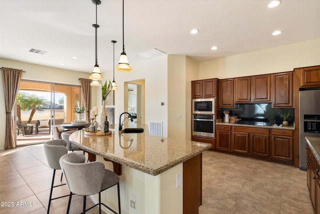 kitchen featuring light stone countertops, sink, appliances with stainless steel finishes, and an island with sink