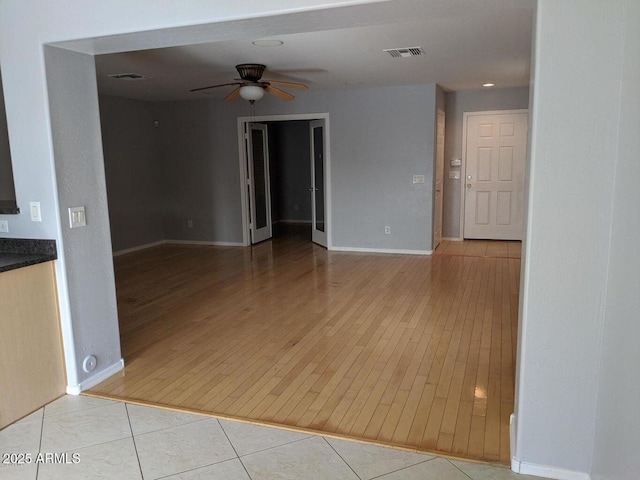 empty room with light tile patterned floors, visible vents, baseboards, and a ceiling fan