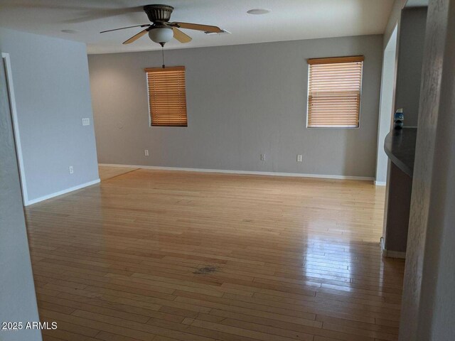 spare room with a ceiling fan, visible vents, light wood-style flooring, and baseboards