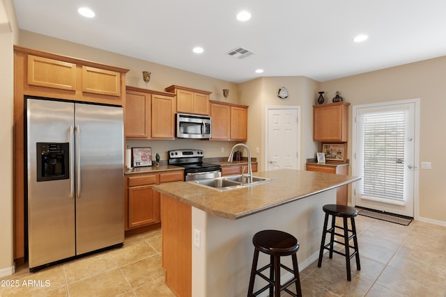 kitchen featuring an island with sink, sink, a kitchen bar, light tile patterned floors, and stainless steel appliances