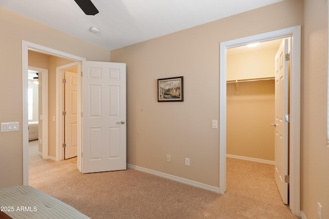 unfurnished bedroom with a walk in closet, light colored carpet, ceiling fan, and a closet