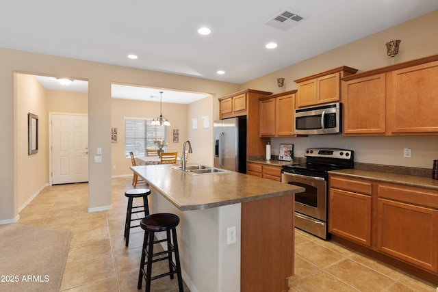 kitchen featuring appliances with stainless steel finishes, a breakfast bar, decorative light fixtures, sink, and a kitchen island with sink