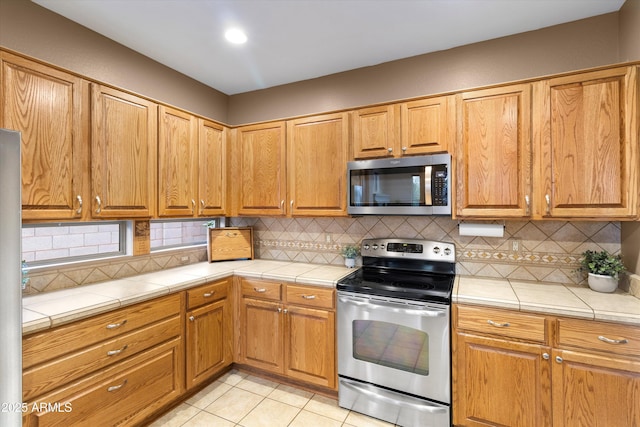 kitchen featuring light tile patterned flooring, appliances with stainless steel finishes, tile countertops, and decorative backsplash