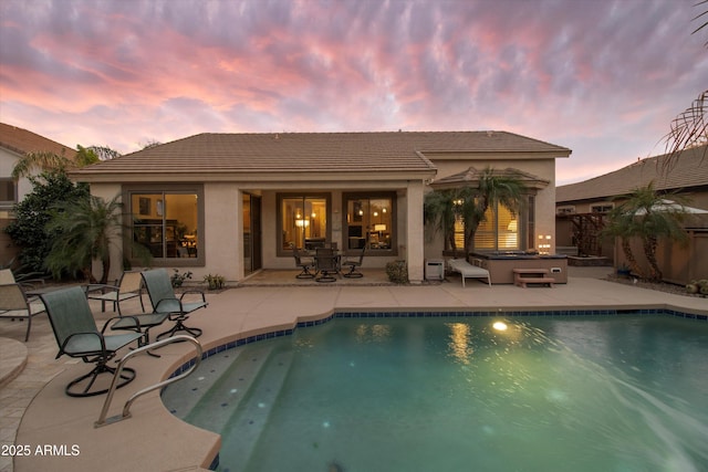 back house at dusk with a swimming pool with hot tub and a patio area