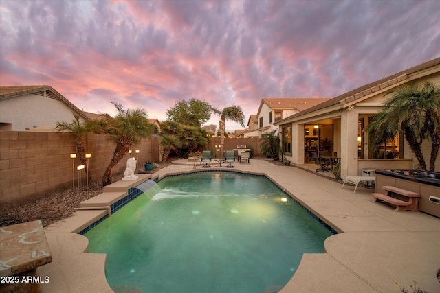 pool at dusk with pool water feature, a jacuzzi, and a patio area