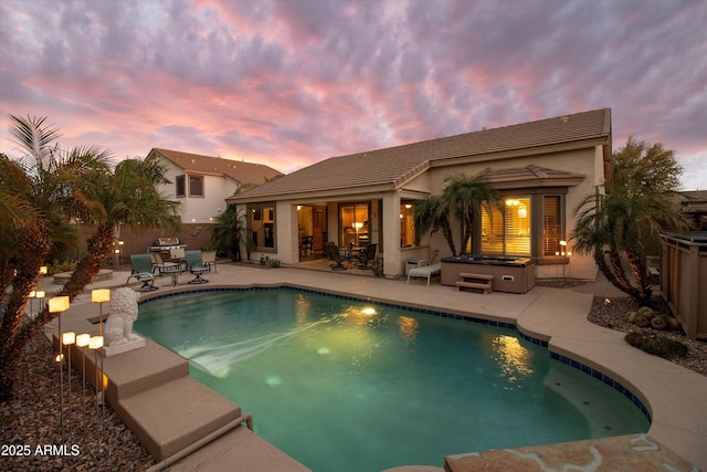 pool at dusk with a hot tub and a patio