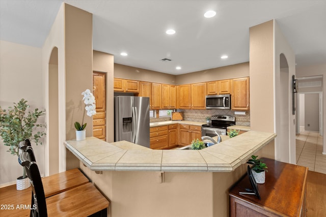 kitchen featuring decorative backsplash, a breakfast bar area, stainless steel appliances, and kitchen peninsula