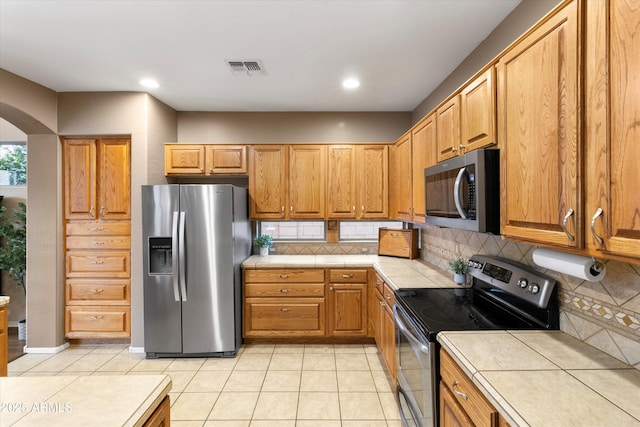 kitchen with appliances with stainless steel finishes, tile countertops, decorative backsplash, and light tile patterned floors