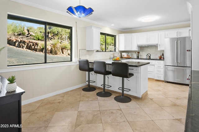 kitchen featuring high end refrigerator, a kitchen breakfast bar, backsplash, decorative light fixtures, and white cabinetry