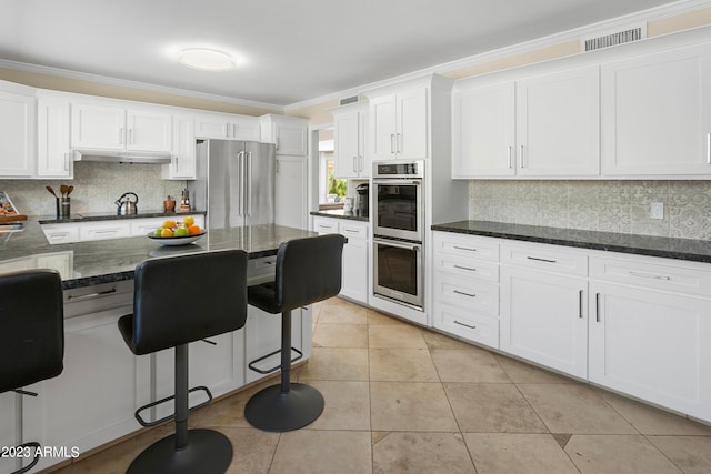 kitchen featuring white cabinetry, stainless steel appliances, dark stone counters, tasteful backsplash, and crown molding