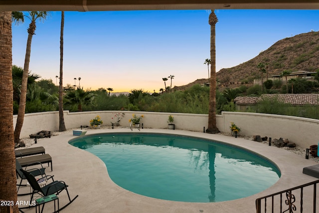 pool at dusk featuring a mountain view and a patio