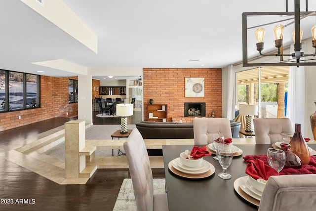 dining area featuring an inviting chandelier, brick wall, a fireplace, and dark hardwood / wood-style floors