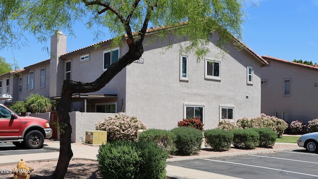 view of side of property with uncovered parking, a chimney, and stucco siding