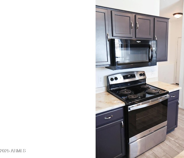 kitchen featuring light countertops, stainless steel range with electric cooktop, black microwave, and light wood finished floors