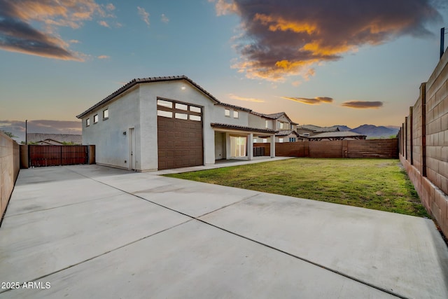 19026 W Becker Ln, Surprise, AZ 85388 - back of property at dusk with a garage, stucco siding, a tile roof, a patio area, and concrete driveway