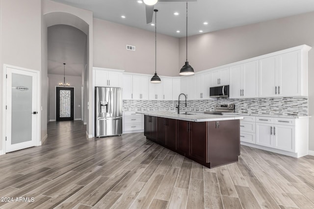 kitchen with white cabinets, decorative backsplash, stainless steel appliances, and a kitchen island with sink