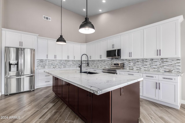 kitchen featuring white cabinetry, sink, stainless steel appliances, a high ceiling, and a center island with sink