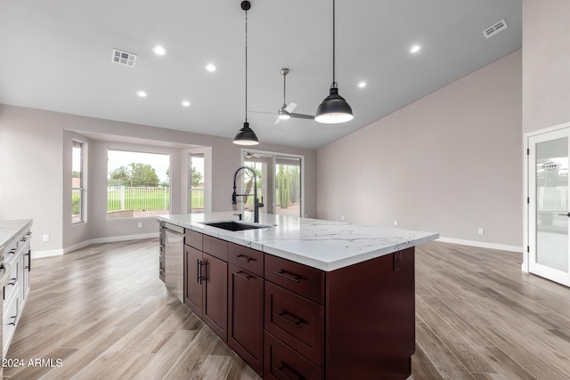 kitchen with a kitchen island with sink, sink, hanging light fixtures, stainless steel dishwasher, and light hardwood / wood-style floors