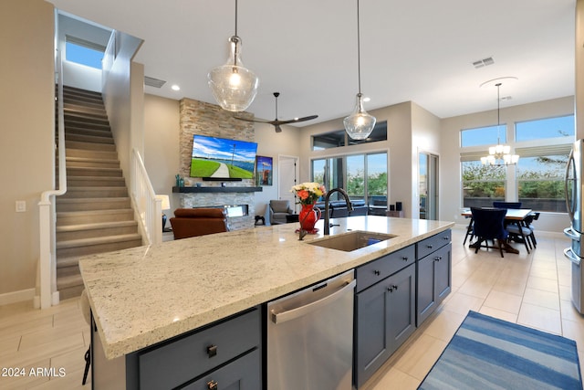 kitchen with sink, appliances with stainless steel finishes, light stone counters, an island with sink, and pendant lighting