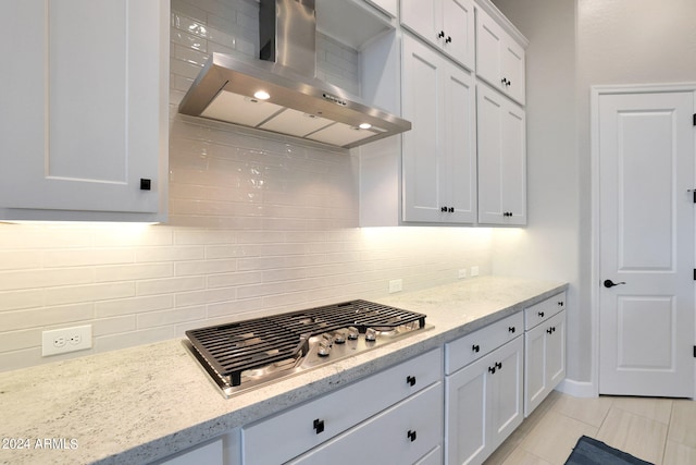 kitchen with decorative backsplash, wall chimney exhaust hood, white cabinets, stainless steel gas cooktop, and light tile patterned floors