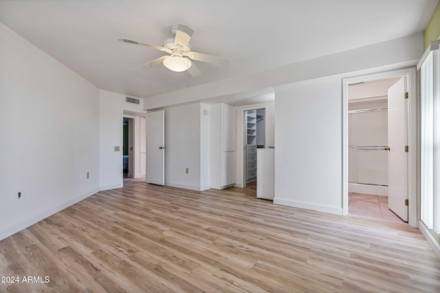 unfurnished bedroom featuring ceiling fan, ensuite bathroom, light wood-type flooring, and a walk in closet