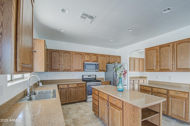 kitchen featuring stainless steel appliances, a sink, visible vents, a center island, and open shelves