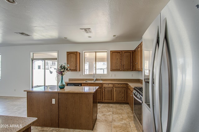 kitchen featuring visible vents, a kitchen island, appliances with stainless steel finishes, brown cabinets, and a sink