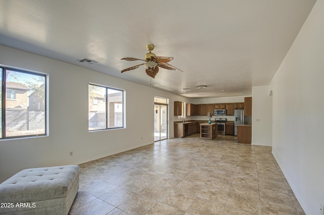 unfurnished living room with arched walkways, visible vents, ceiling fan, a sink, and baseboards