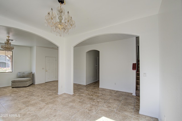 unfurnished room featuring a chandelier, arched walkways, and baseboards