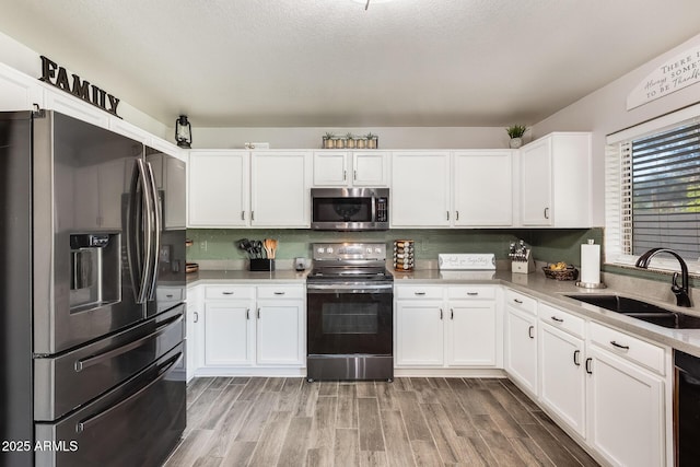 kitchen with white cabinetry, sink, wood-type flooring, a textured ceiling, and appliances with stainless steel finishes