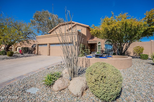 view of front of home with stucco siding, concrete driveway, a patio area, fence, and a garage