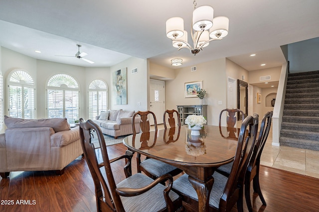 dining room featuring stairs, ceiling fan with notable chandelier, dark wood finished floors, and visible vents