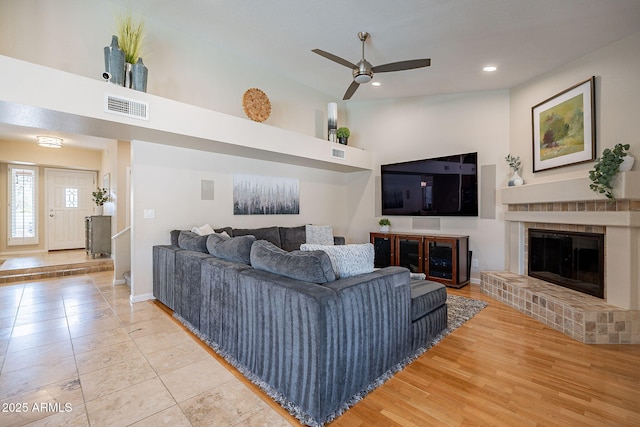 living room featuring light tile patterned floors, a high ceiling, a fireplace, visible vents, and a ceiling fan