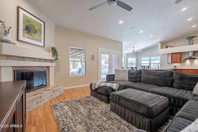 living area featuring a fireplace, vaulted ceiling, light wood-style flooring, and baseboards