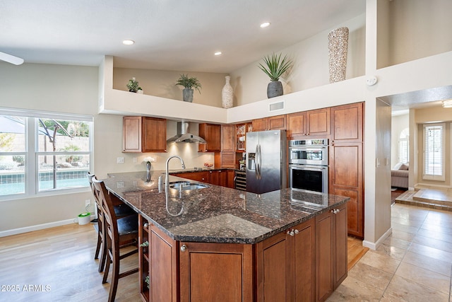 kitchen with brown cabinets, stainless steel appliances, a kitchen bar, visible vents, and wall chimney exhaust hood