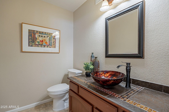 half bathroom with toilet, a textured wall, vanity, and baseboards