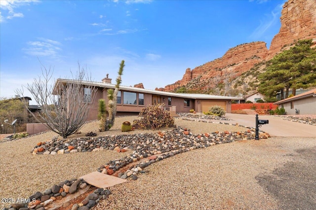 view of front of home featuring a chimney, concrete driveway, an attached garage, a mountain view, and fence