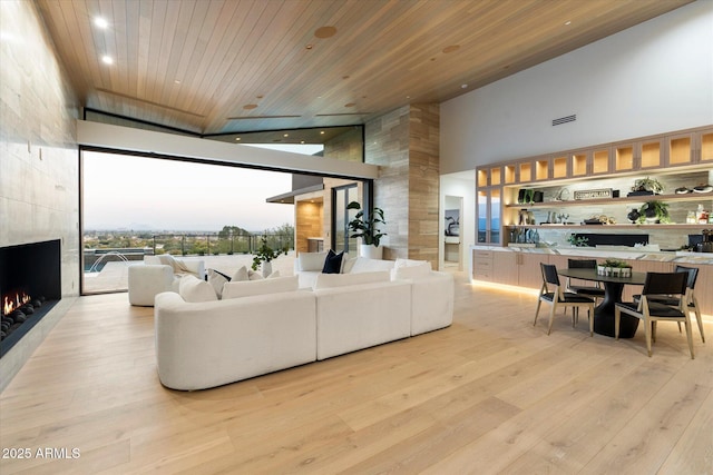 living room with wood ceiling, a wall of windows, a high ceiling, a high end fireplace, and light hardwood / wood-style floors