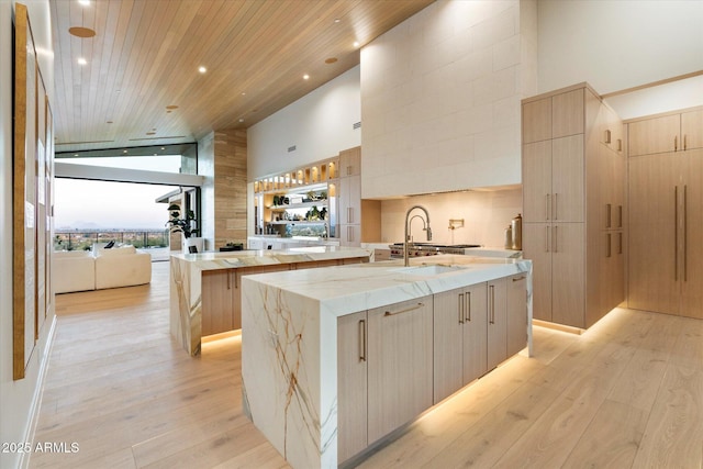 kitchen with wooden ceiling, light hardwood / wood-style floors, a high ceiling, and a center island with sink