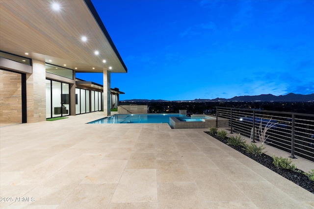 pool at dusk featuring an in ground hot tub, a mountain view, and a patio area