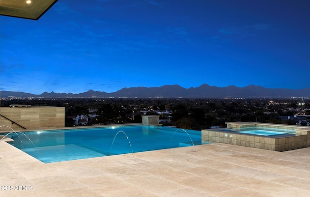 pool at dusk with an in ground hot tub, pool water feature, and a mountain view