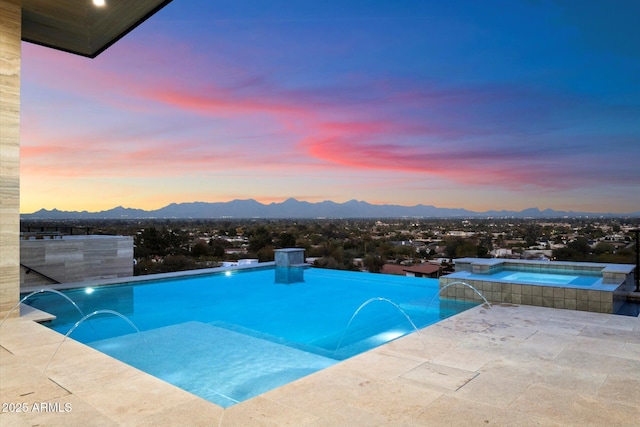 pool at dusk featuring pool water feature, an in ground hot tub, and a mountain view