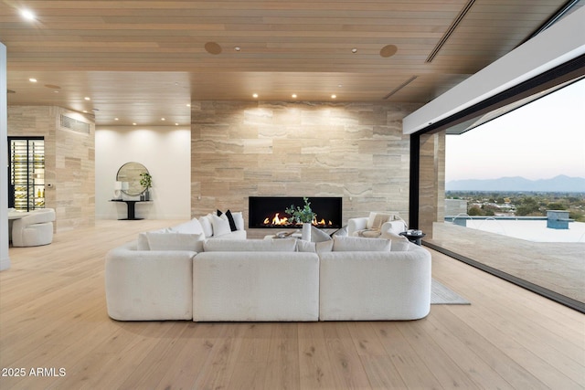 living room with wood ceiling, a large fireplace, a healthy amount of sunlight, and light hardwood / wood-style flooring