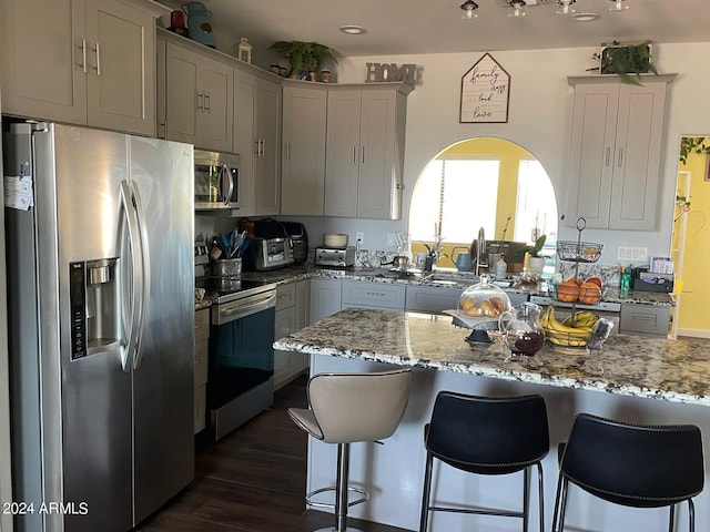 kitchen with a breakfast bar area, light stone countertops, appliances with stainless steel finishes, dark wood-type flooring, and sink