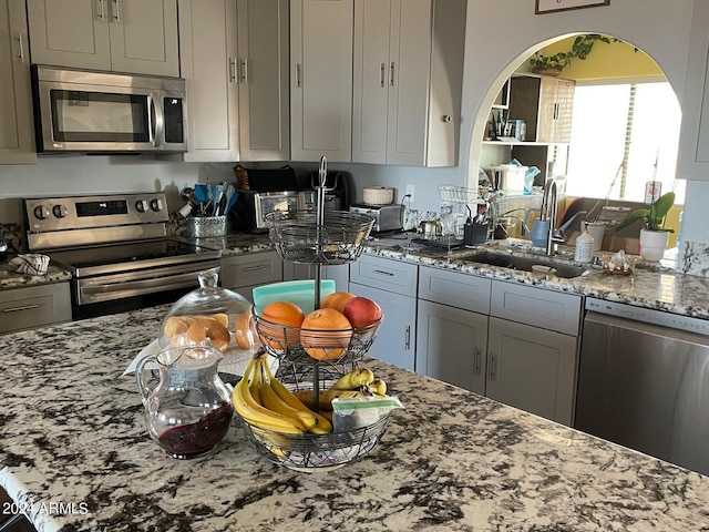 kitchen with gray cabinets, appliances with stainless steel finishes, light stone counters, and sink